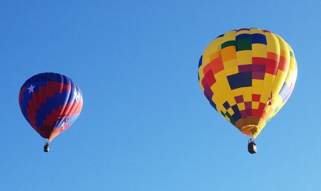 A red and blue hot air balloon and yellow multicolored hot air balloon flying in a clear blue sky