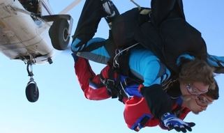 Two people tandem skydiving with an airplane in the background