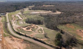 A winding dirt motocross track cutting through grassy, wooded terrain.