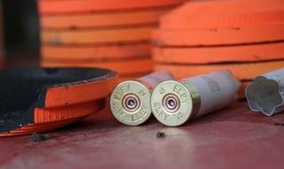 Two red shotgun shells lying in front of stacked orange clay targets on a flat surface.