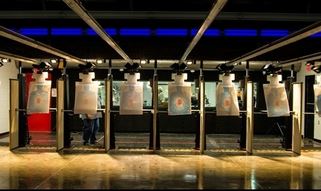 People at an indoor shooting range standing behind individual lanes, aiming at bullseye targets down