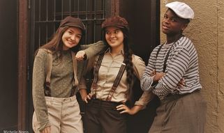Three people in vintage clothing pose in front of a beige wall with barred windows.