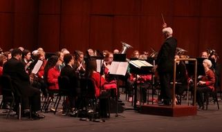 Orchestra performing in a concert hall, with musicians in formal attire led by a conductor on stage