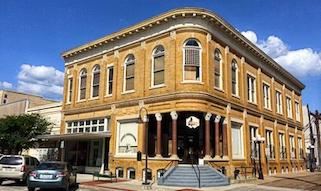 Historic two-story brick building with arched windows and columned entrance, set on a street corner