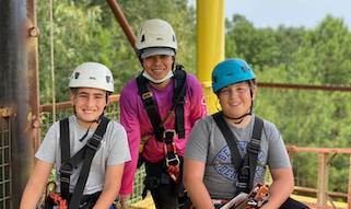 2 boys and a woman smiling with helmets, trying zip lining at Billy Bob's Zipline